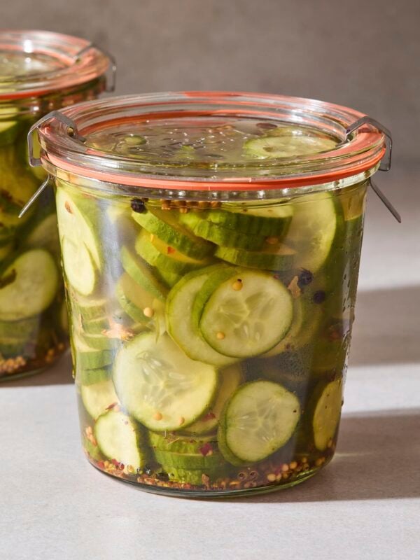 Glass jar filled with sliced sweet pickles with pickling spice in jar.