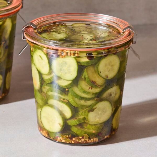 Two jars of sweet pickles with pickling spices in brine.