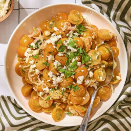 White serving bowl with tomato salad made with Sungold tomatoes and feta on top.
