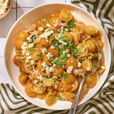 White serving bowl with tomato salad made with Sungold tomatoes and feta on top.
