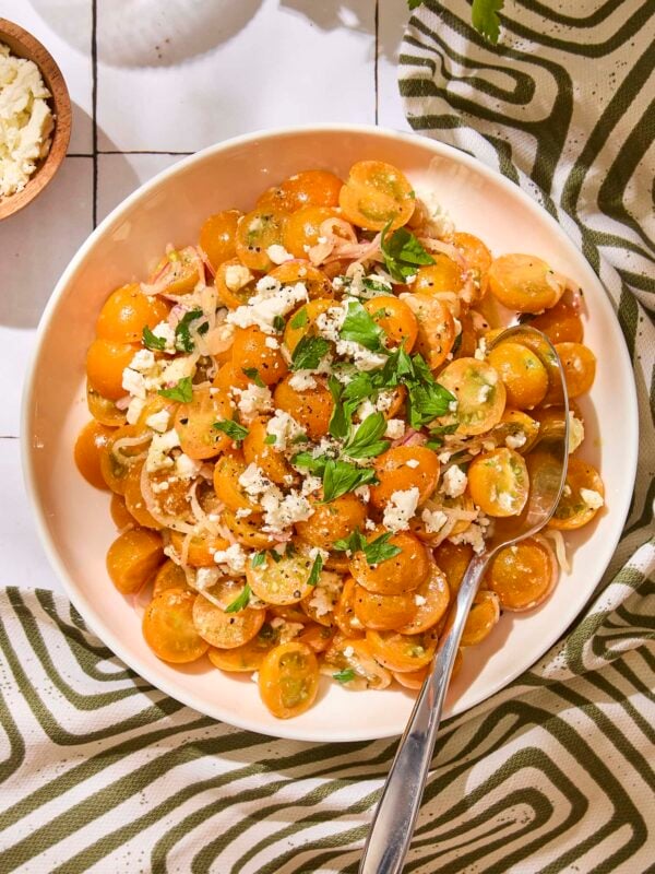White serving bowl with tomato salad made with Sungold tomatoes and feta on top.