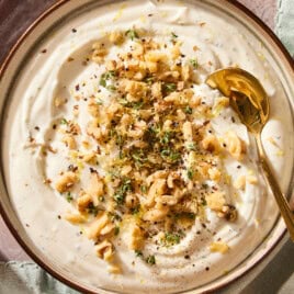 Whipped ricotta dip in a bowl topped with chopped walnuts and thyme with a spoon scooping out serving.