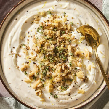 Whipped ricotta dip in a bowl topped with chopped walnuts and thyme with a spoon scooping out serving.