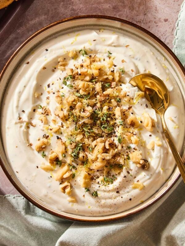 Whipped ricotta dip in a bowl topped with chopped walnuts and thyme with a spoon scooping out serving.