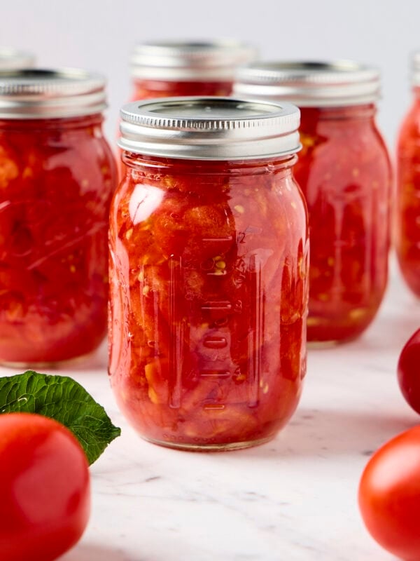 Tomatoes sit next to a glass jar of preserved tomatoes.