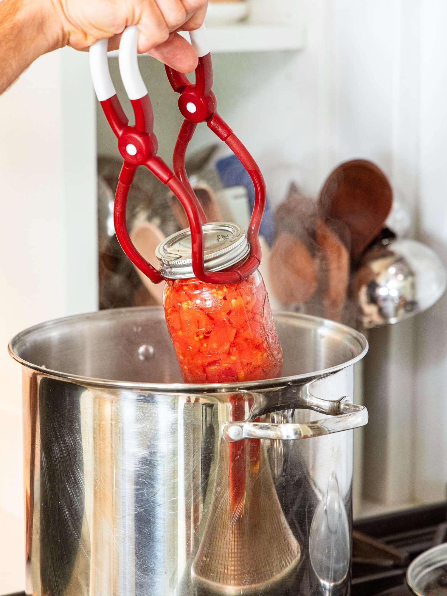 Pulling a jar of diced tomatoes out of a water bath canner.