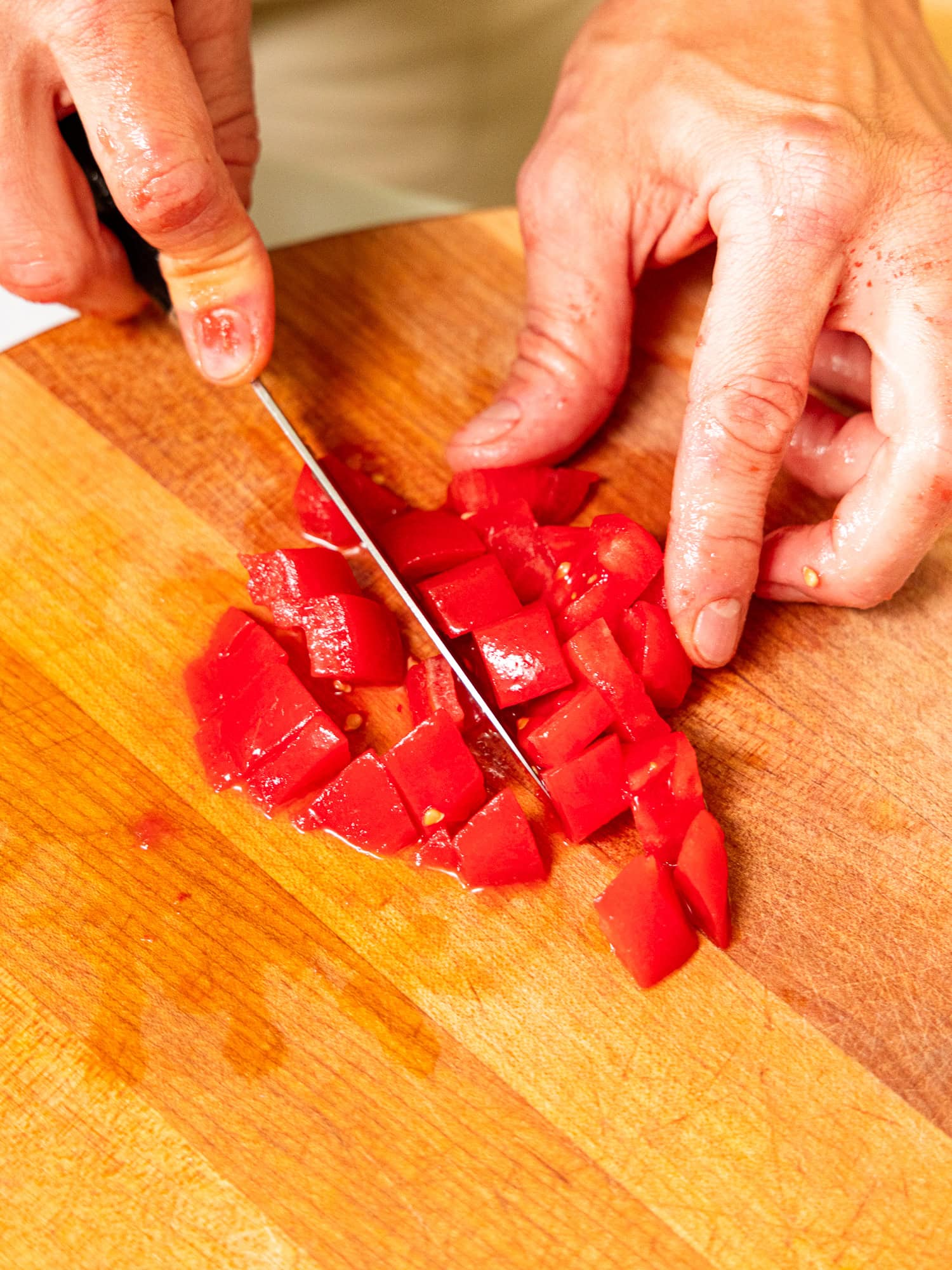 Dicing tomatoes on a wood cutting board.