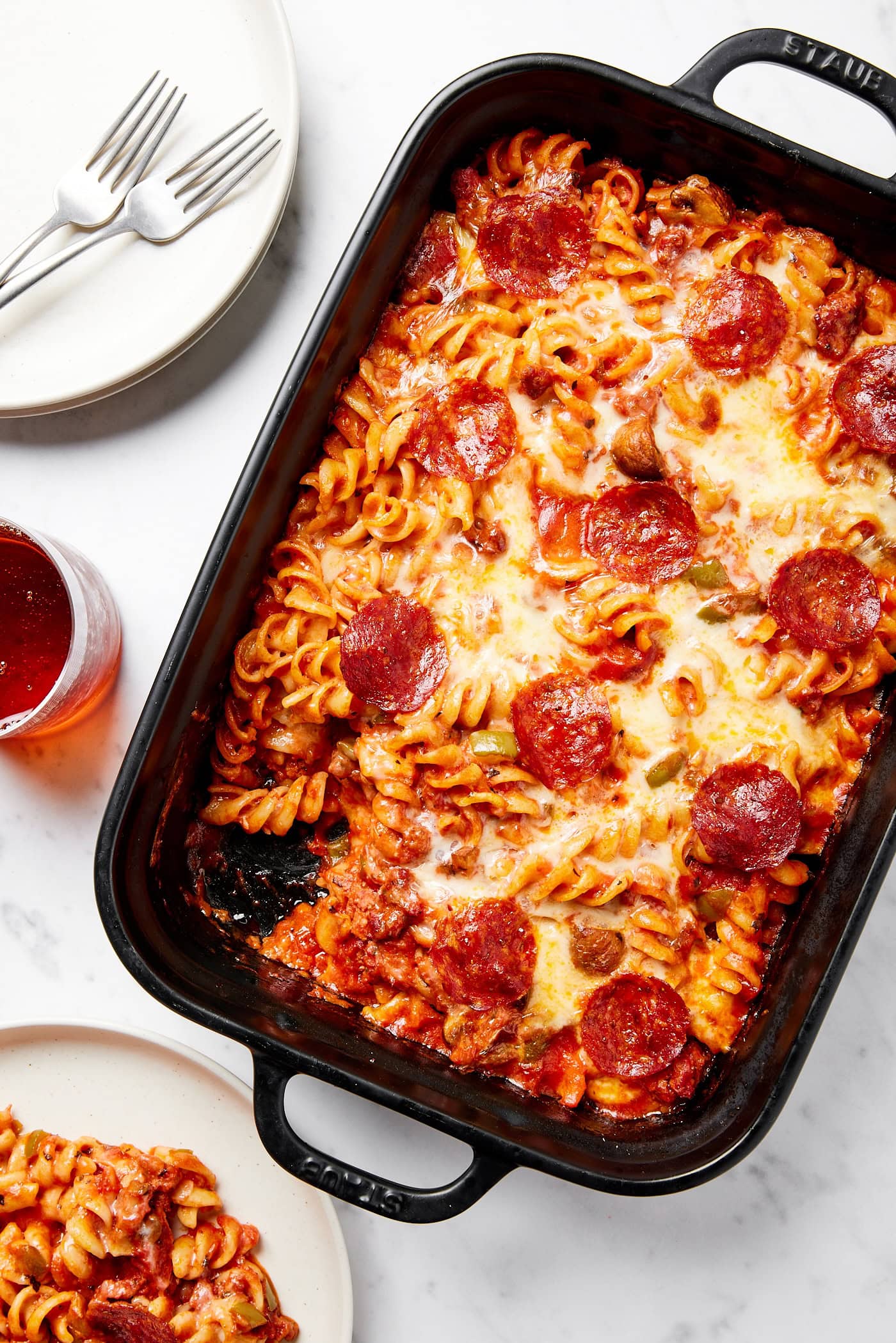 Black baking dish filled with casserole with cheese and pepperonis on top with a serving taken out.