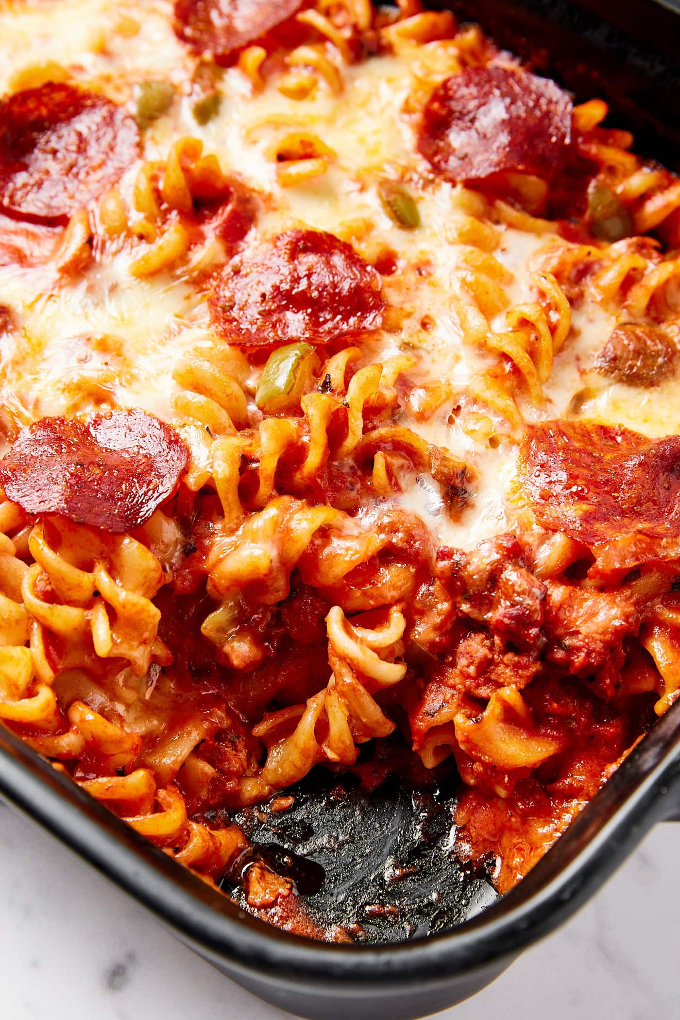Pasta inside a casserole dish with tomato sauce, cheese, and pepperonis.
