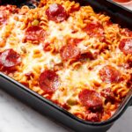 Baked pizza casserole with cheese and pepperonis on top in black baking dish.