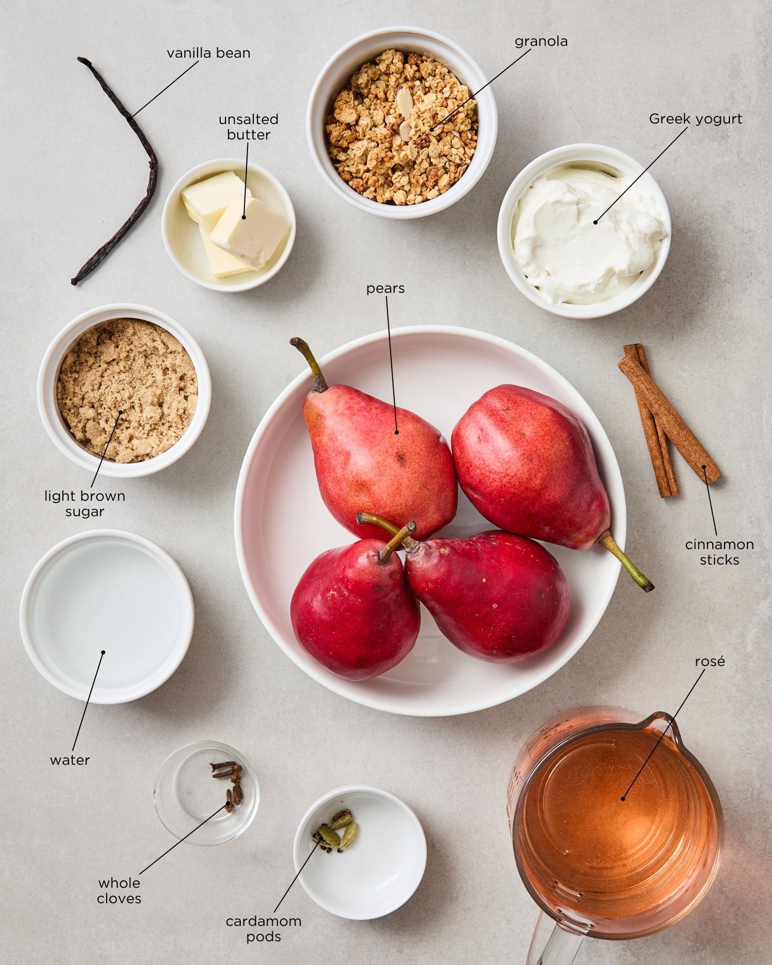 Concrete surface filled with ingredients needed to make poached pears including spices, pears, wine, and more.