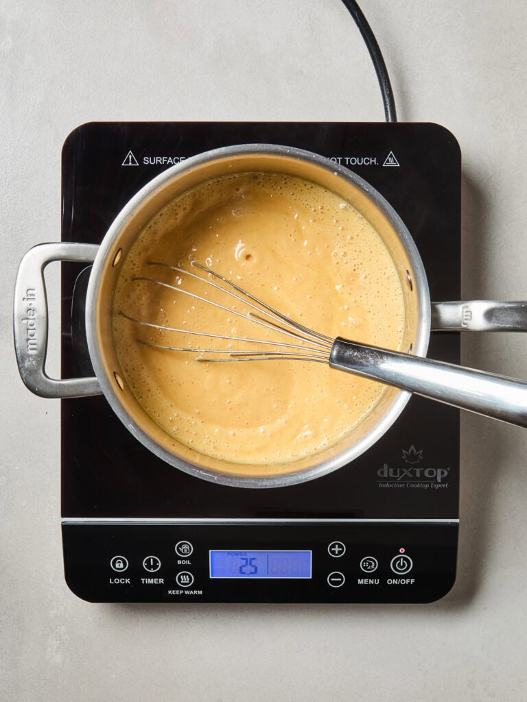 Ice cream mixture with an egg slurry cooking down on a stove.