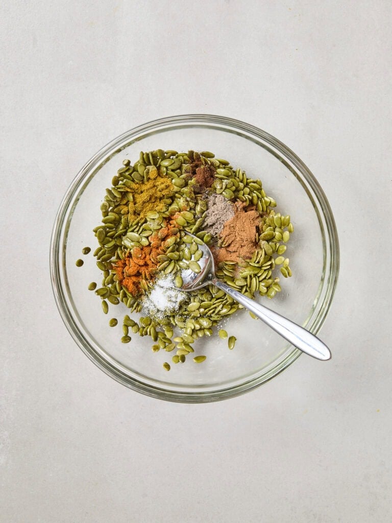 Spices on top of raw pepitas in a small bowl.