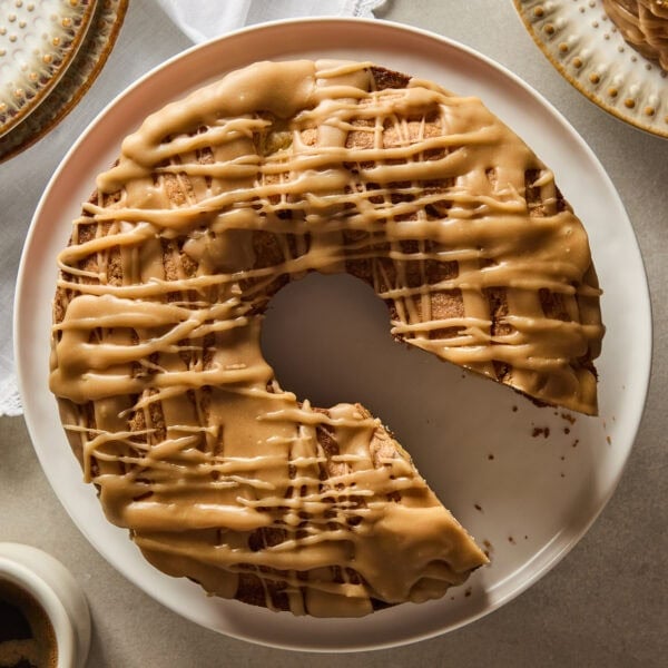 Circular apple cake with slice cut out on a cake plate with glaze on top.