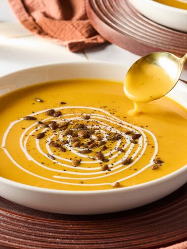 Bowl filled with squash soup with spoon dipping in to get a serving.