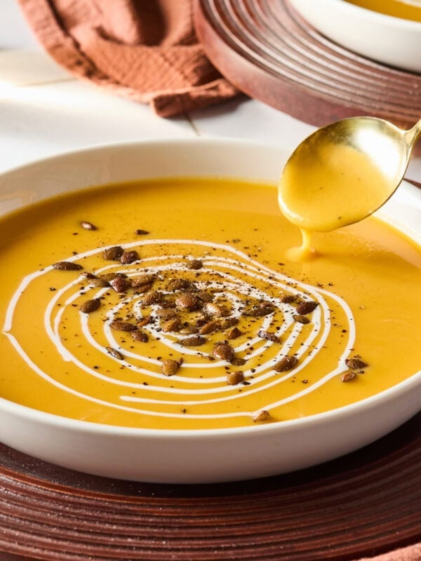 Bowl filled with squash soup with spoon dipping in to get a serving.