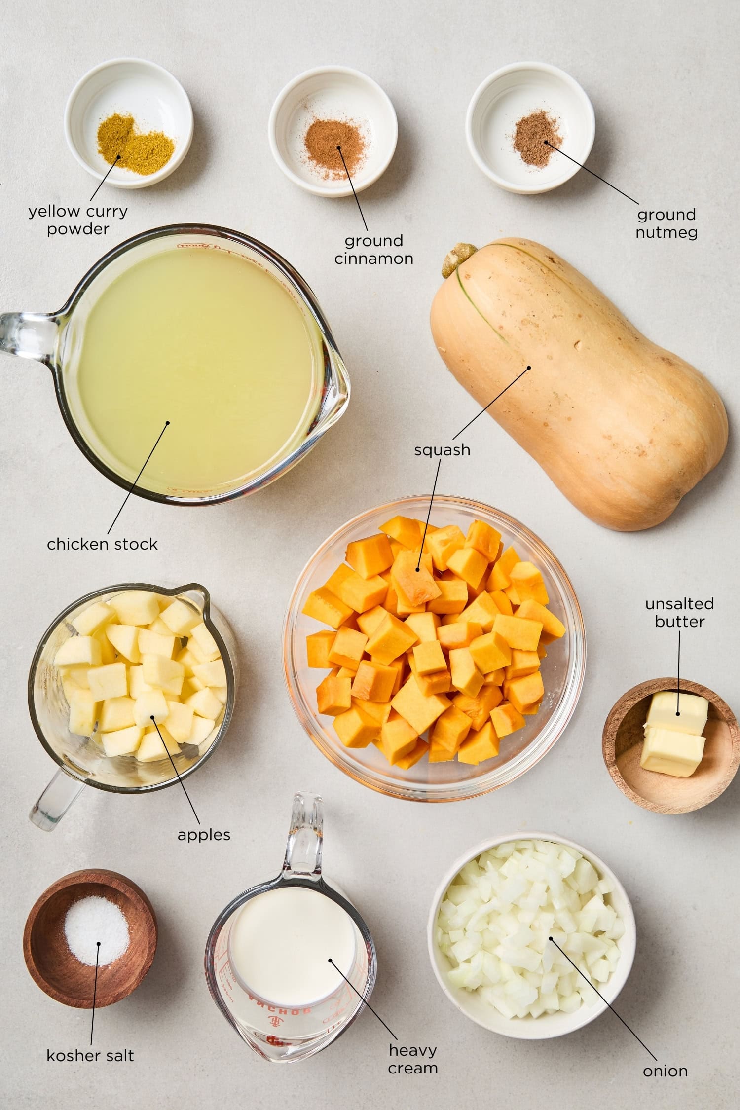 Concrete surface with ingredients needed for squash soup, including squash, apples, stock, spices, and more.