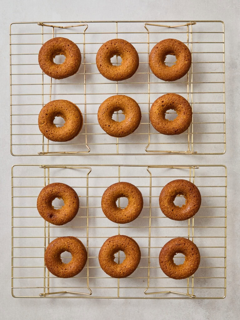 Baked pumpkin donuts cooling on wire racks.