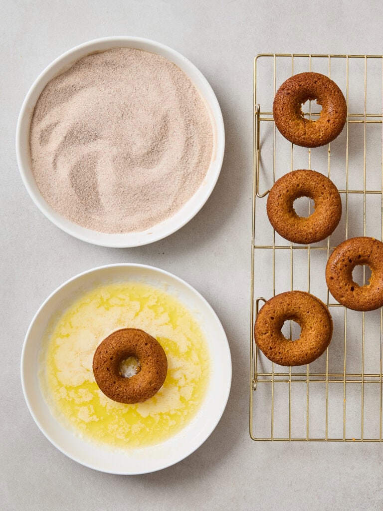 Baked pumpkin spice donuts getting dipped in butter prior to getting coated in cinnamon sugar.