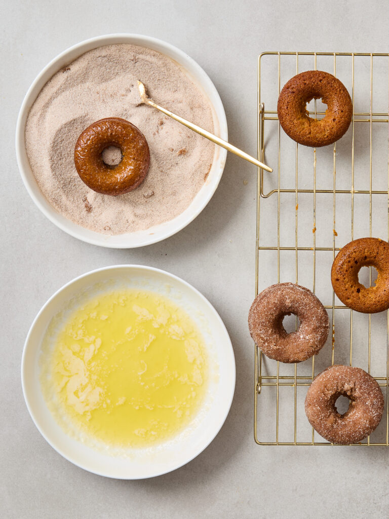 Dipping pumpkin donuts in cinnamon sugar after getting a butter coating.