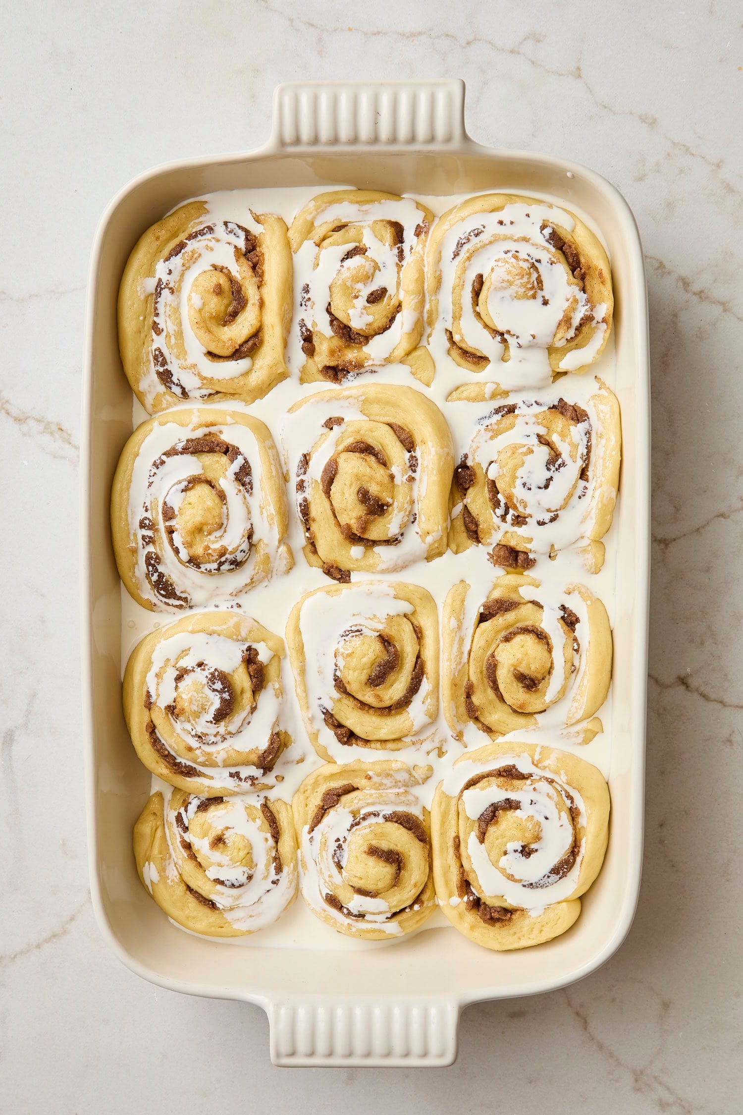 Unbaked cinnamon rolls with heavy cream poured on top before going into the oven.