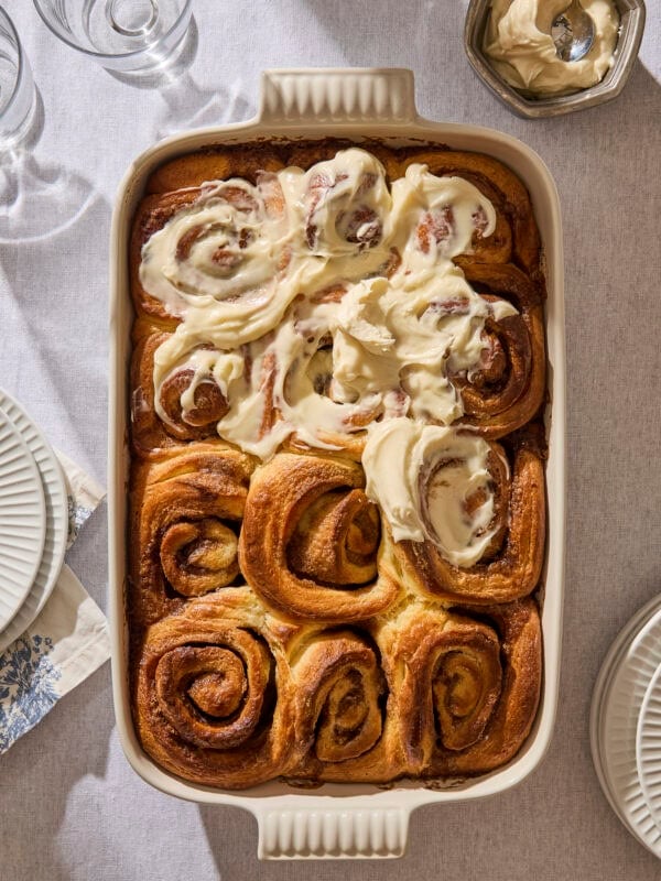 Baking pan filled with partially frosted brioche cinnamon rolls.