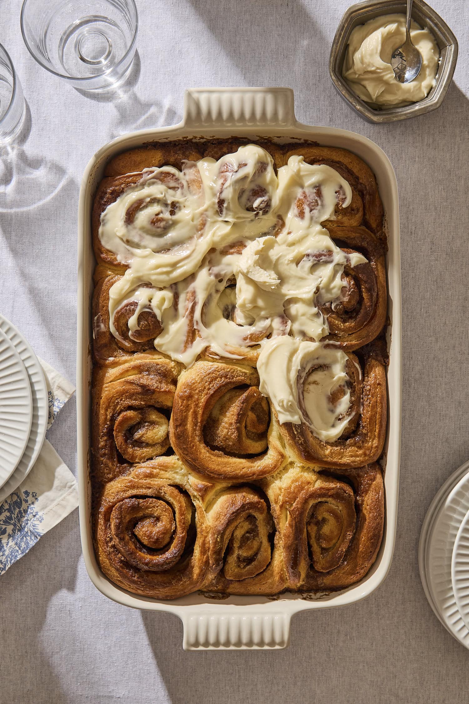 Baking pan filled with partially frosted brioche cinnamon rolls.
