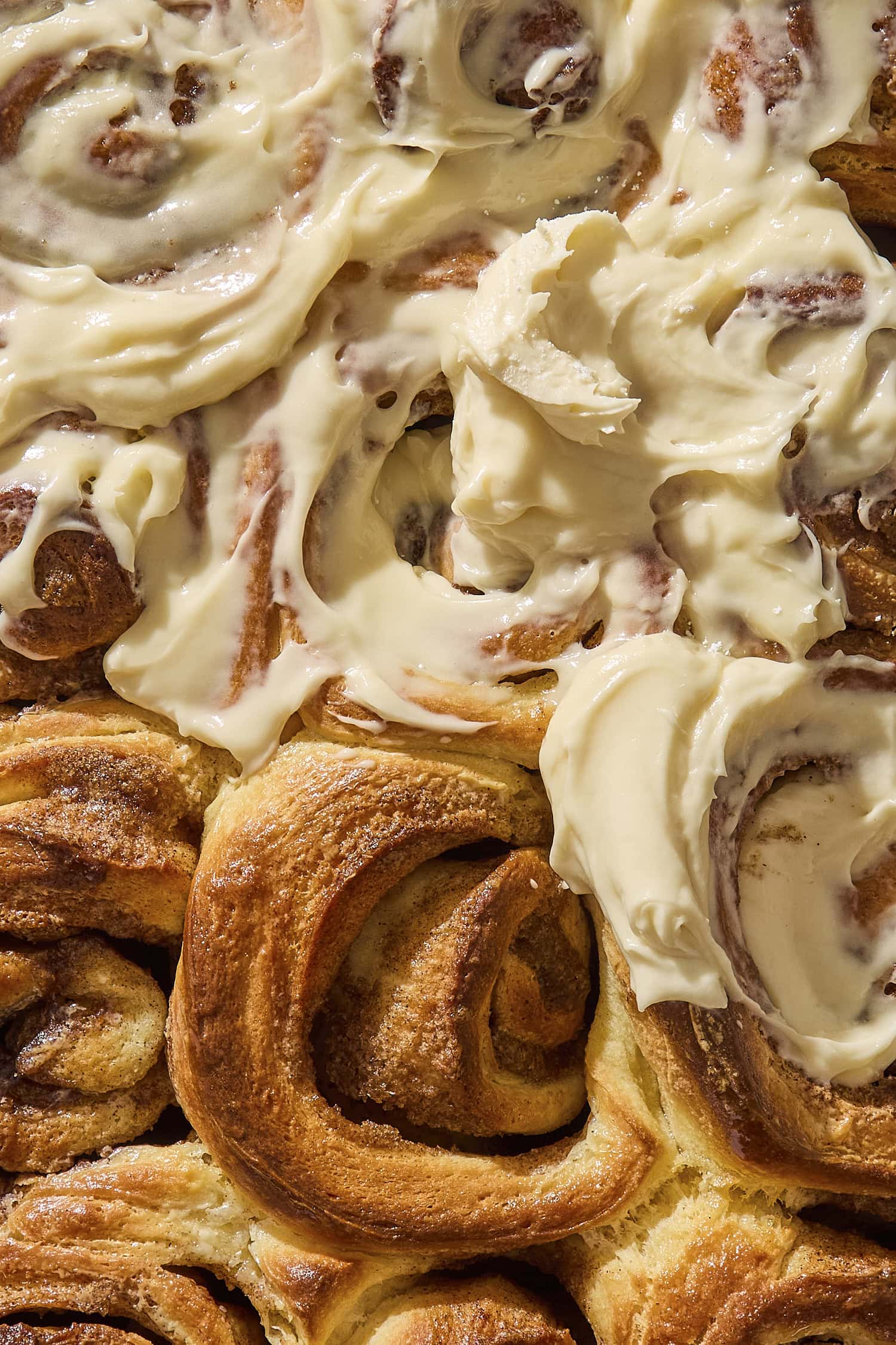 Baked brioche cinnamon rolls with cream cheese frosting partially covering rolls.