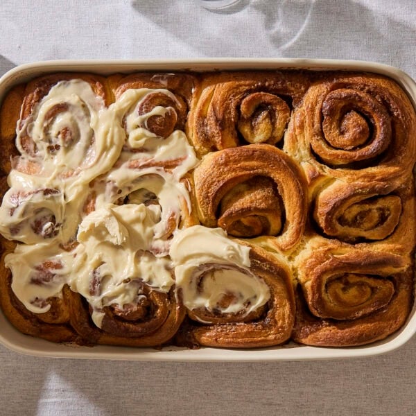 Baked cinnamon rolls with cream cheese frosting covering half of the rolls.