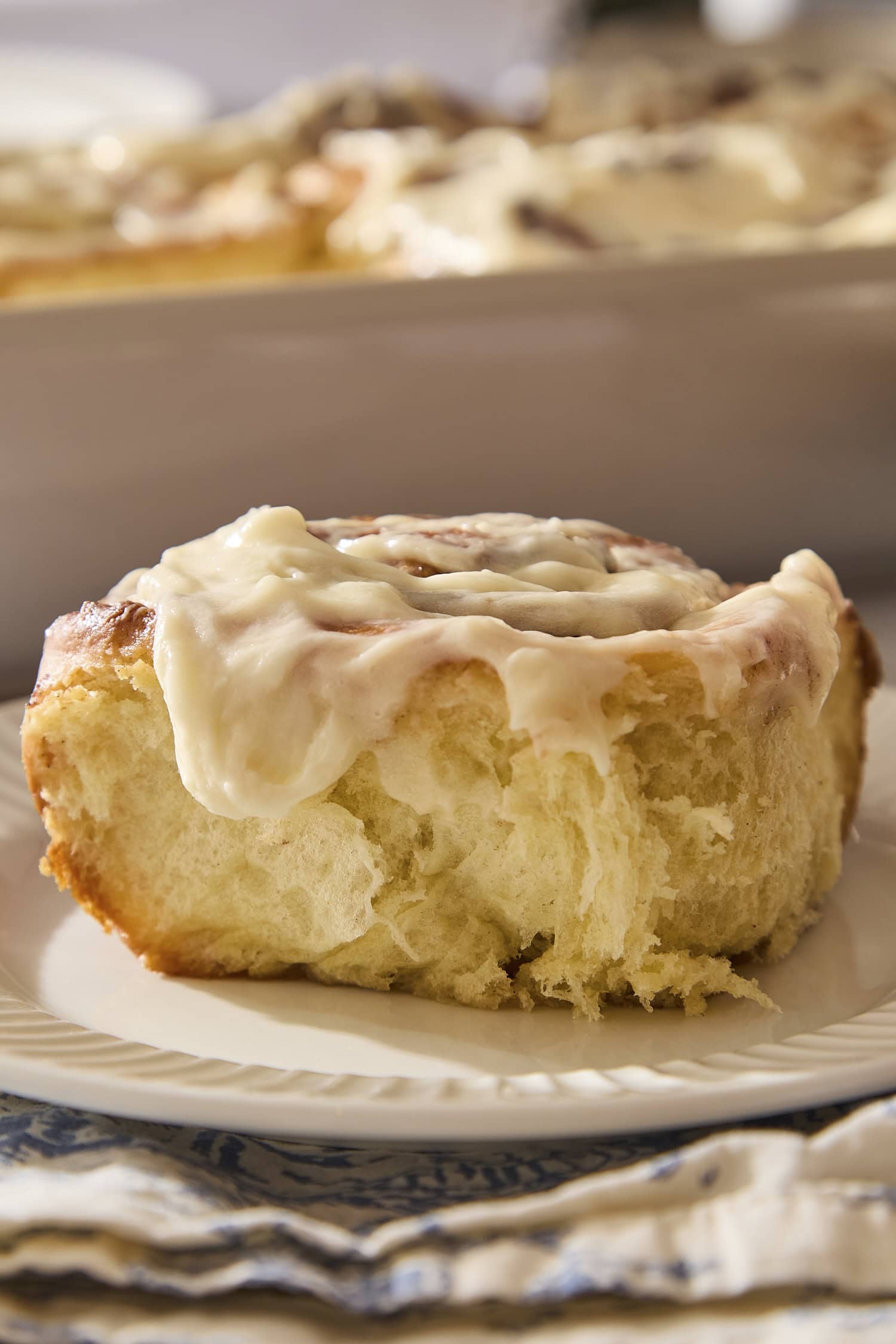 Plate with single cinnamon roll topped with cream cheese frosting.