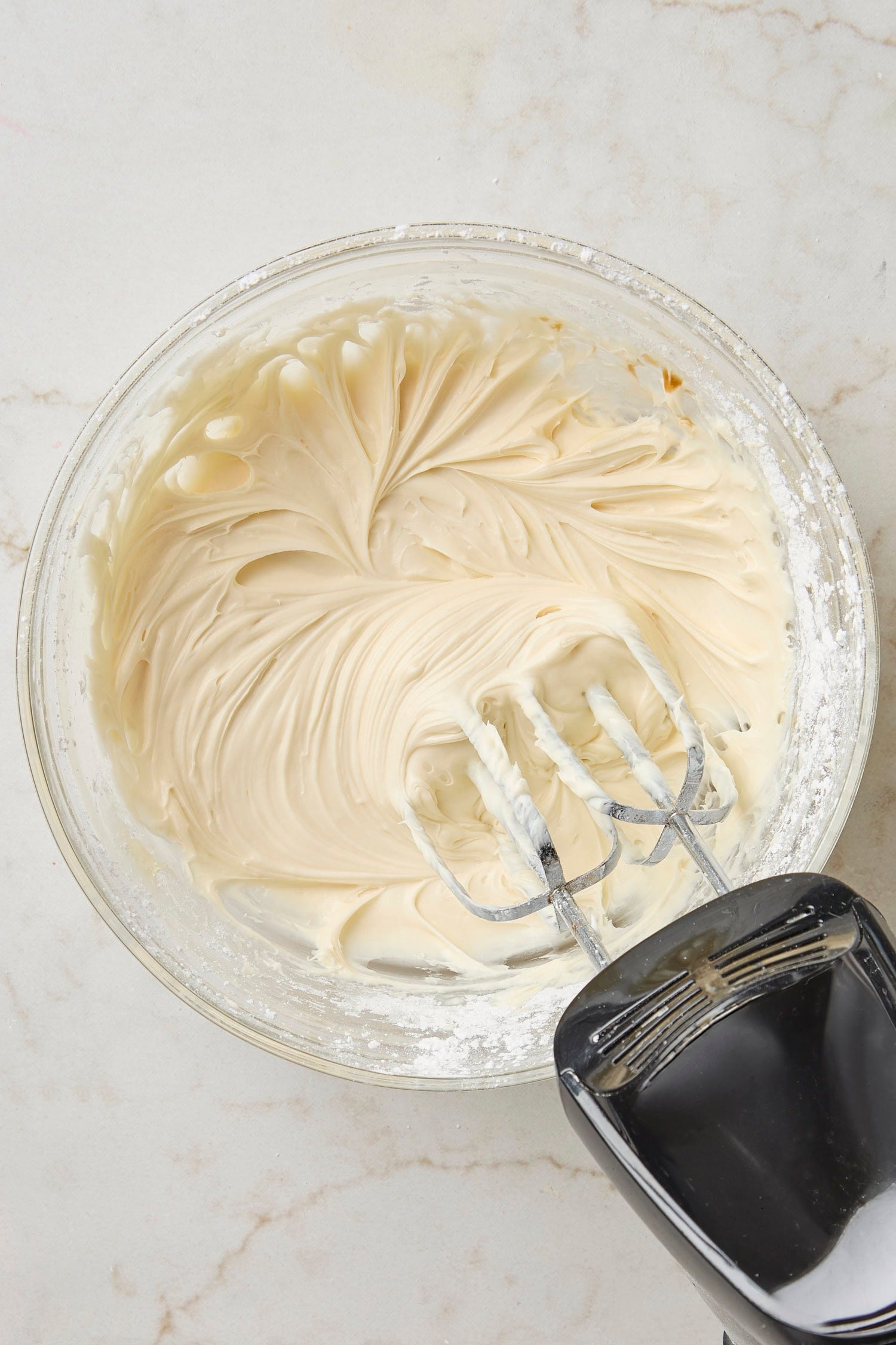 Glass bowl with cream cheese frosting after being mixed together.