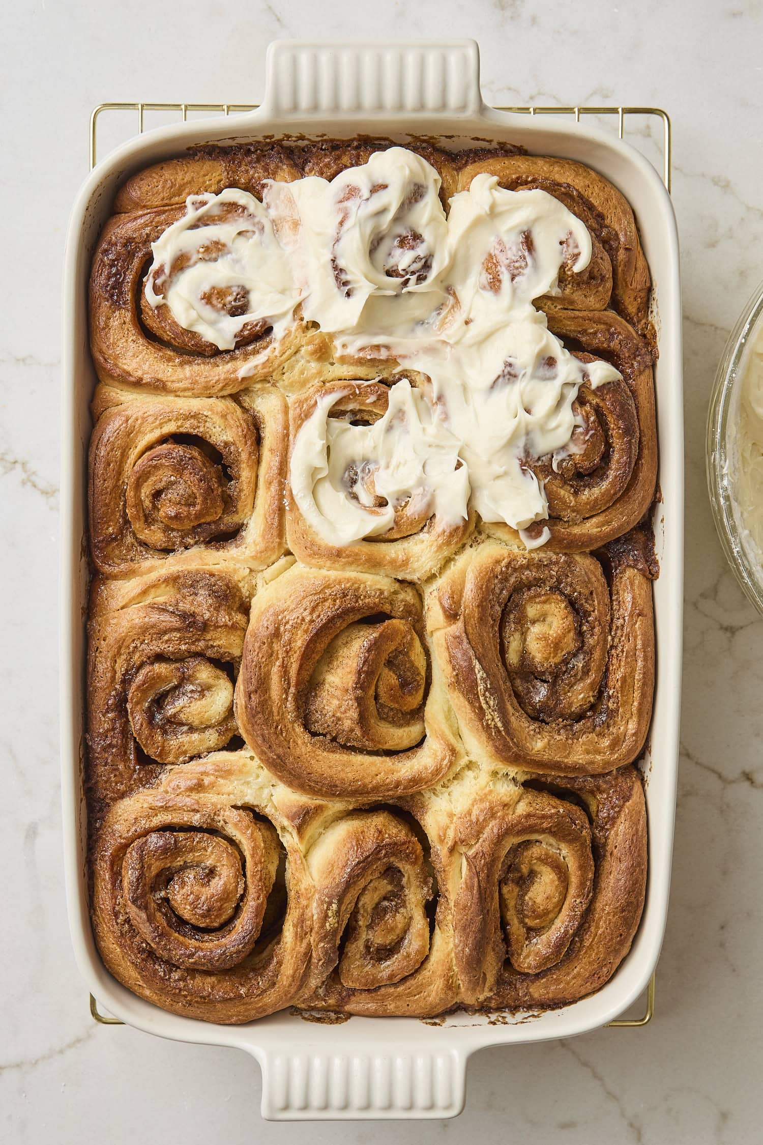 Baked cinnamon rolls partially frosted with cream cheese frosting.