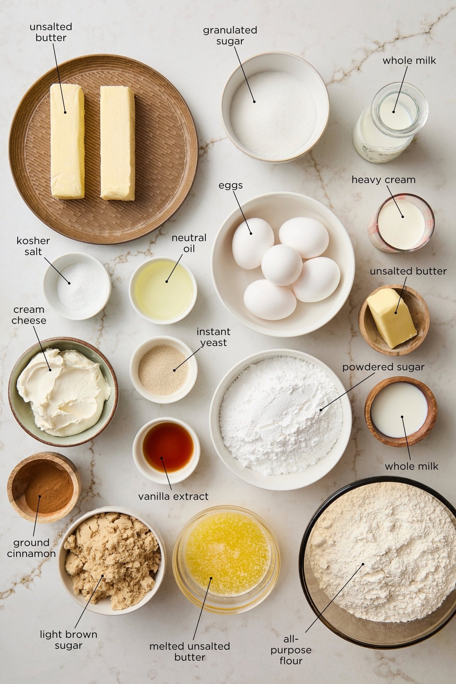 Countertop surface with ingredients needed for cinnamon rolls including butter, flour, sugar, and more.
