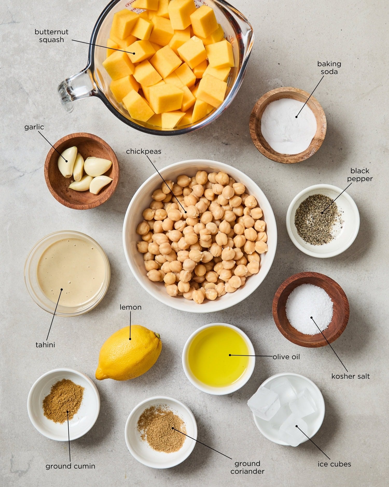 Concrete surface with ingredients for squash hummus recipe including chickpeas, squash, spices, and more.