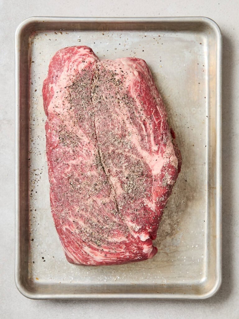 Chuck roast rests on a baking sheet after being seasoned.