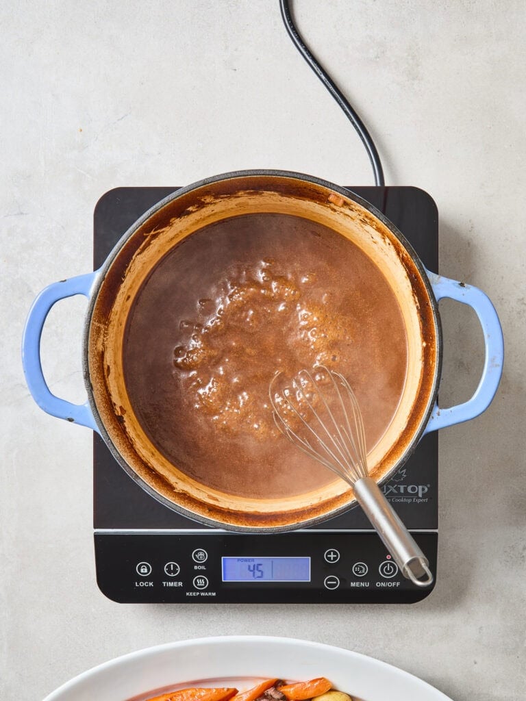 Gravy for a pot roast simmering on a stove.