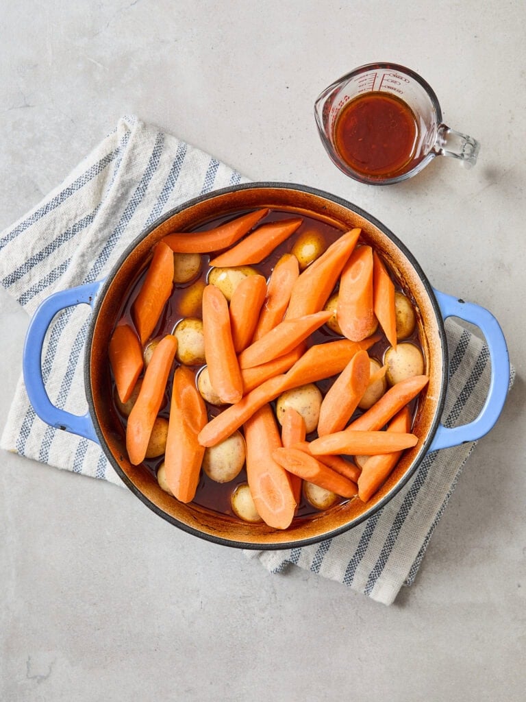 Adding carrots and onions to a Dutch oven partially through cooking a chuck roast.