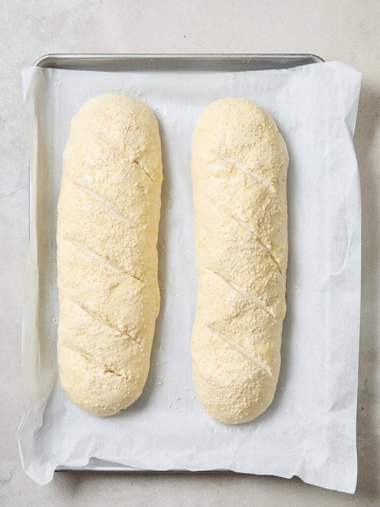 Two loaves of bread with relief cuts on a baking sheet.