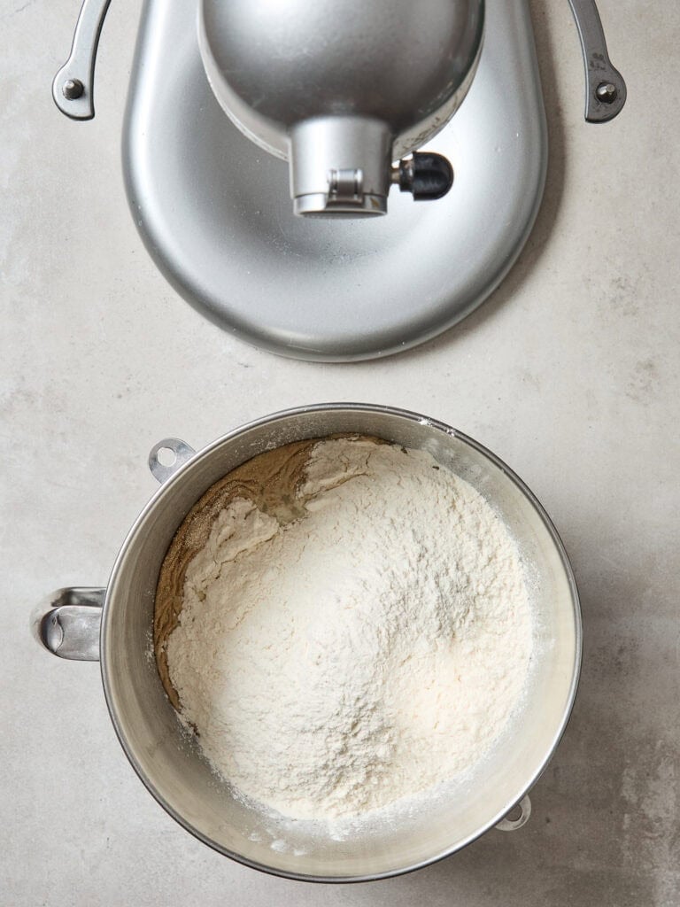 Adding flour to a metal bowl to create bread dough.