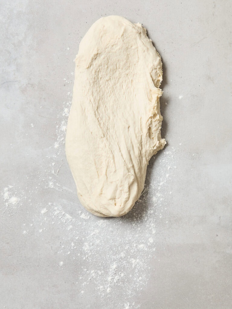 Bread dough stretched out on a floured surface.