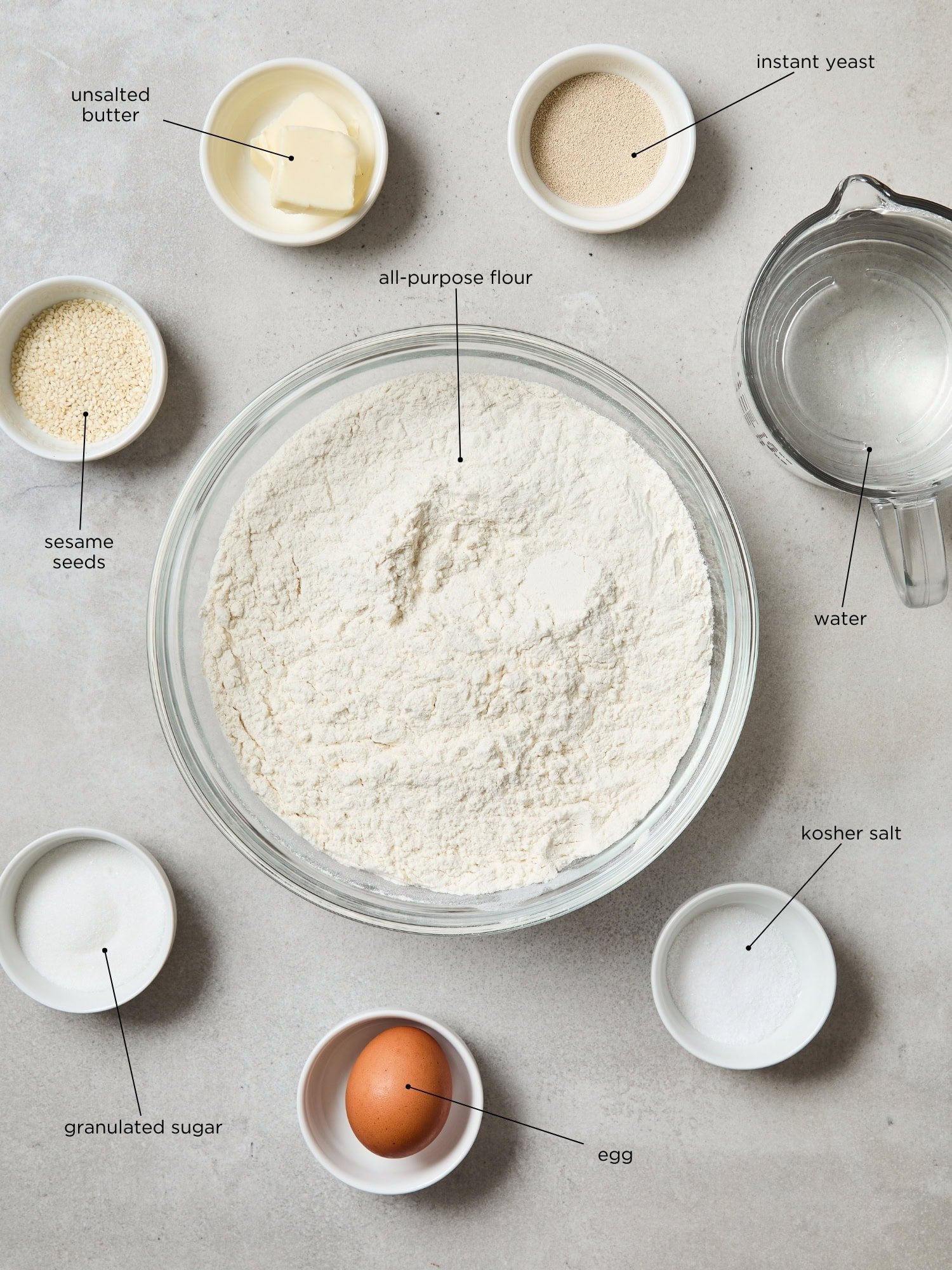 Concrete surface with ingredients needed to make French bread including water, flour, sugar, salt, and more.