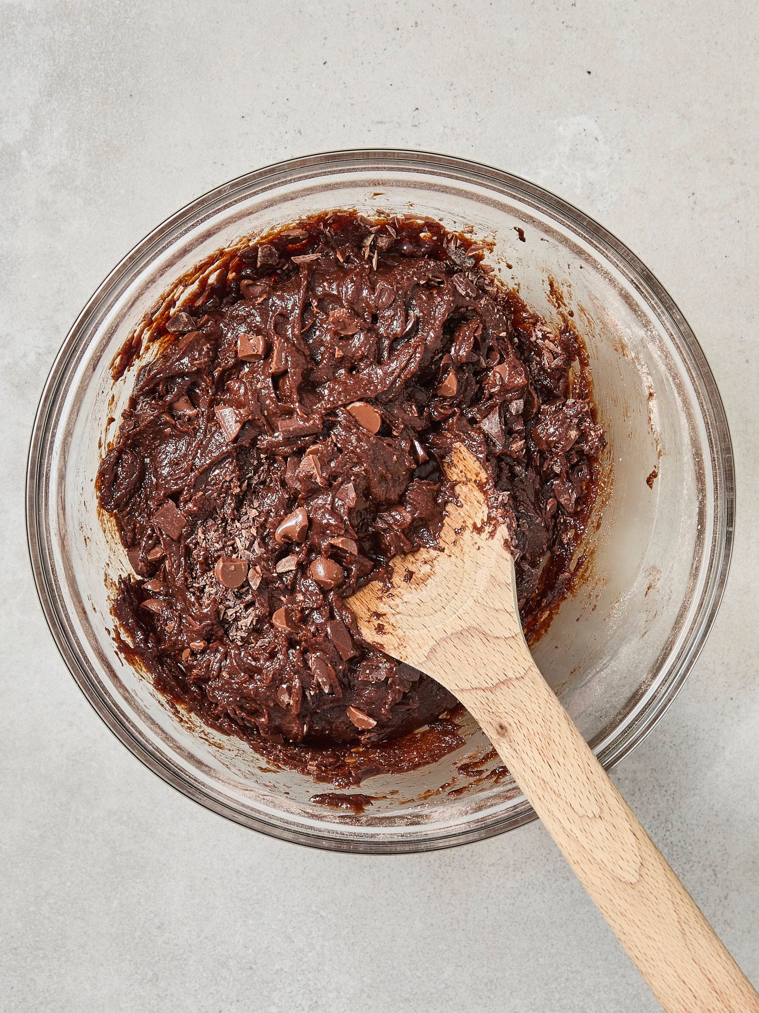 Glass bowl with pieces of chocolate being mixed in for brownies.