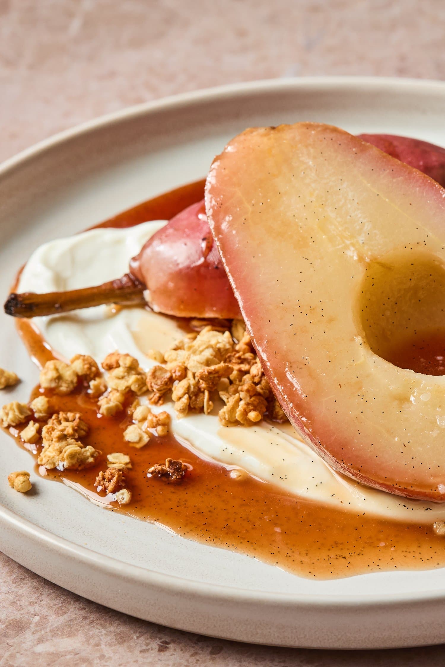 Poached pears served on a plate with syrup and a sprinkle of granola.