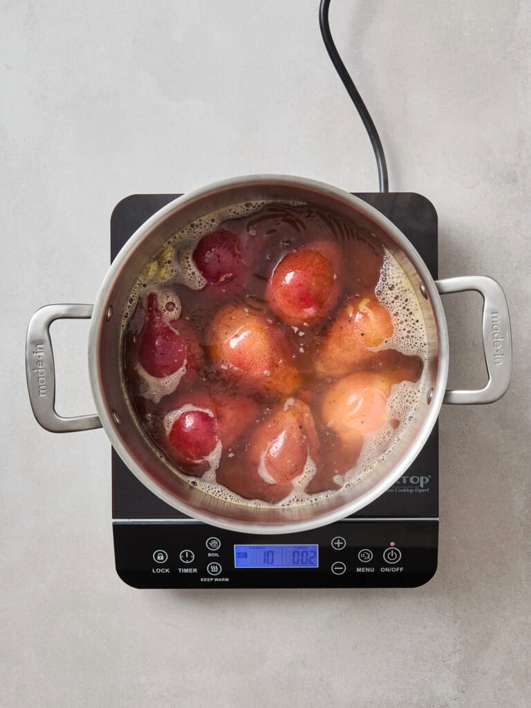 Pears near the end of cooking in poaching liquid on a stovetop.