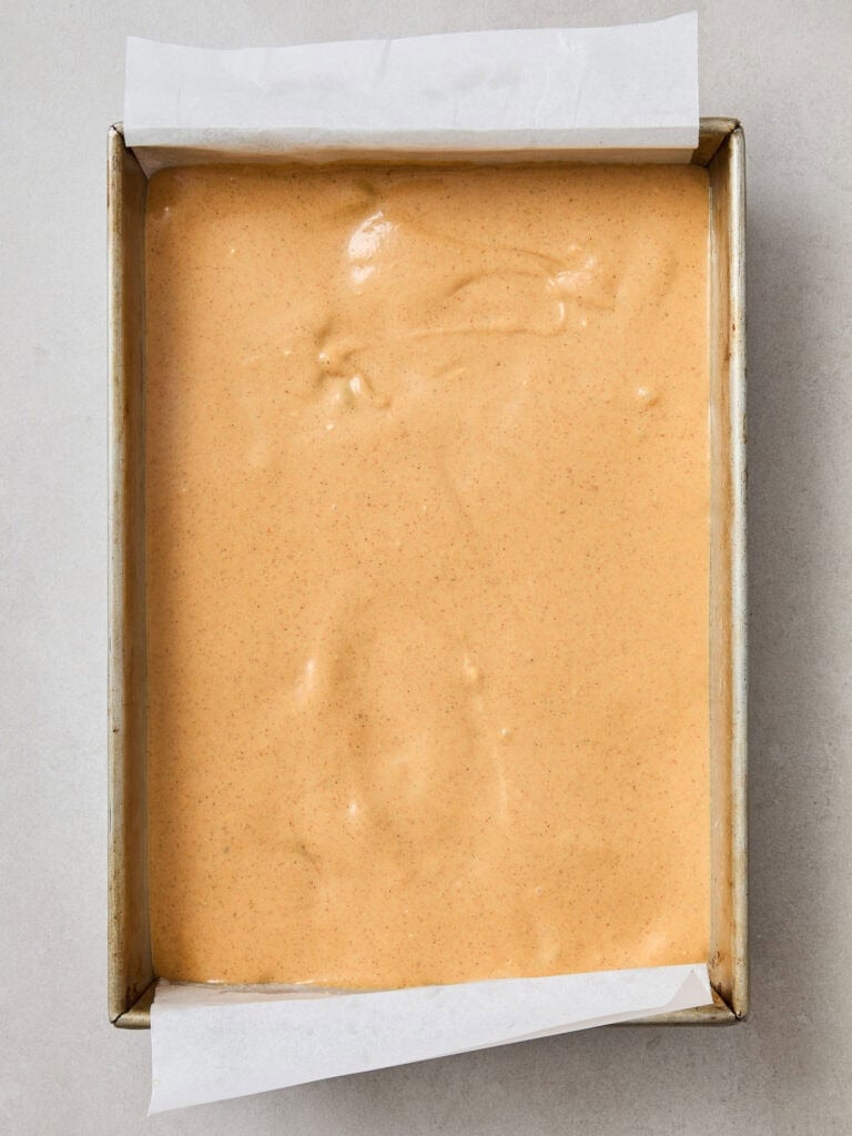 A layer of pumpkin cheesecake overtop a brownie layer in a pan.