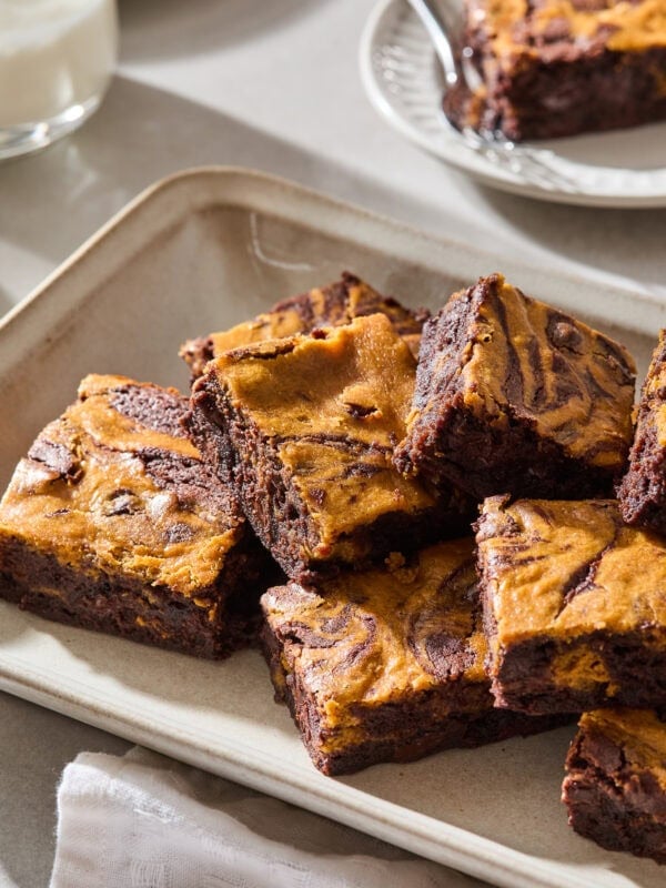 A stack of pumpkin cheesecake brownies sits on a platter.