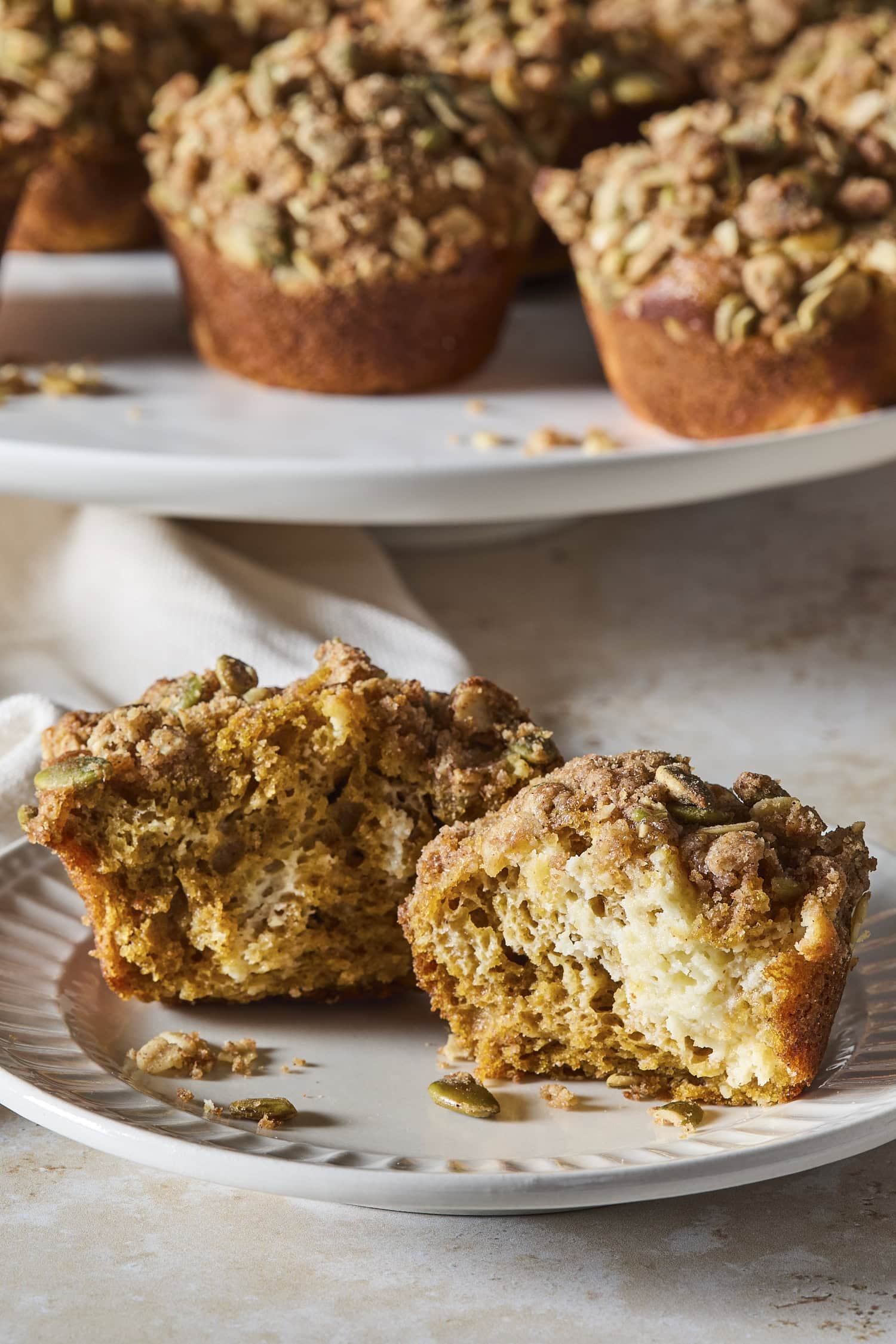 A pumpkin cheesecake muffin cut in half on a plate, showing pumpkin batter with cheesecake.