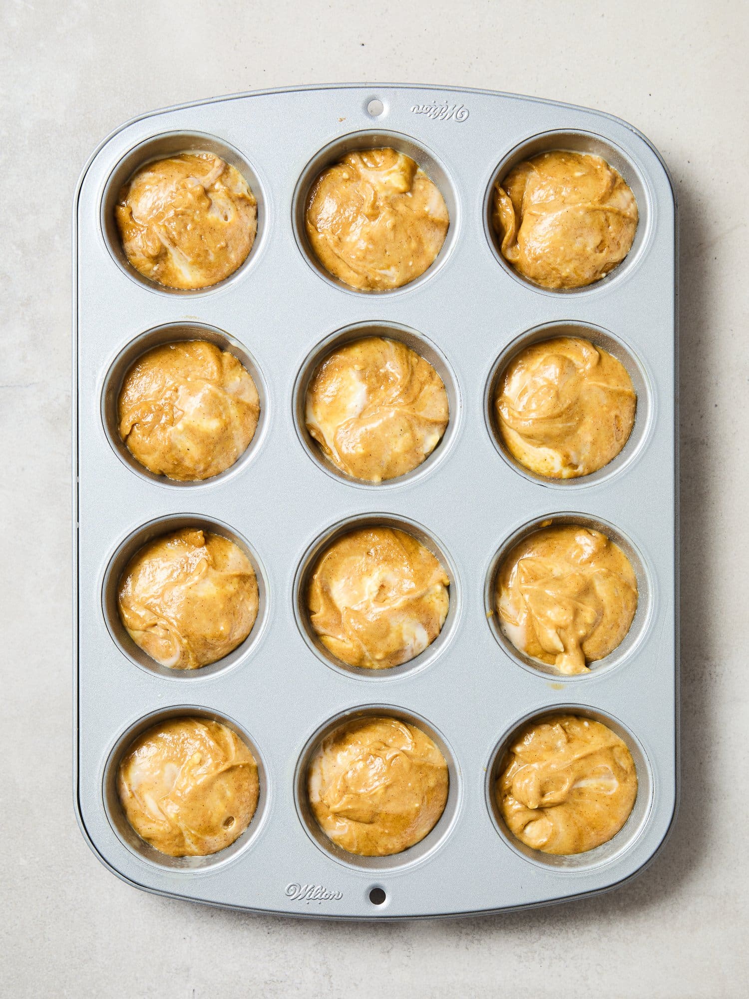 Adding pumpkin cheesecake batter to a muffin tin.