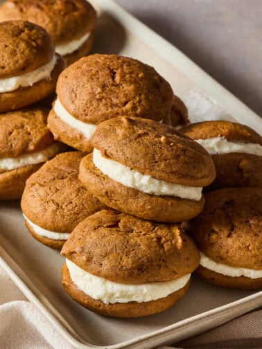 A pile of pumpkin whoopie pies on a baking sheet.