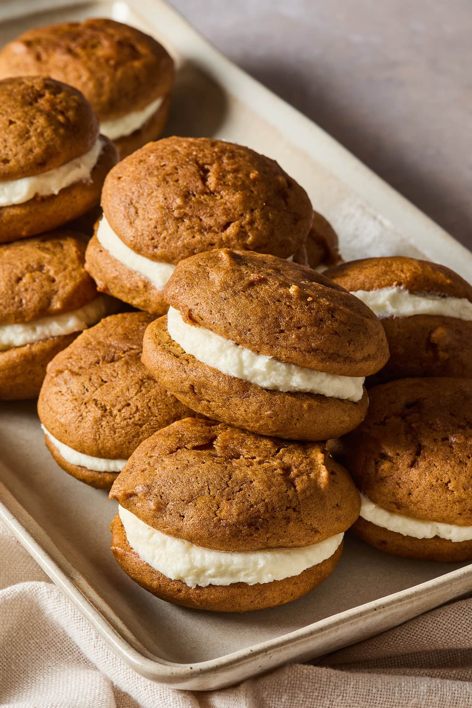 A pile of pumpkin whoopie pies on a baking sheet.